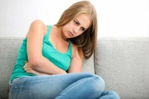 woman hunched over in discomfort on couch canadianpharmacymeds.com