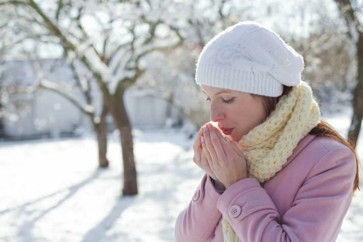 Woman breathing on hands while outside in winter CanadianPharmacyMeds.com